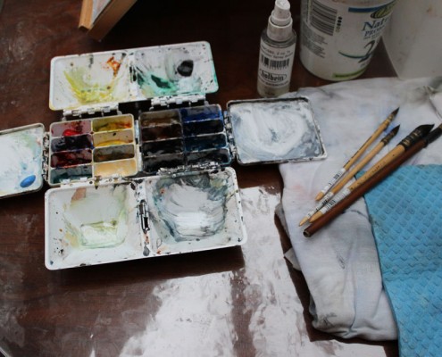 Set of watercolour paints with four paint brushes next to it.