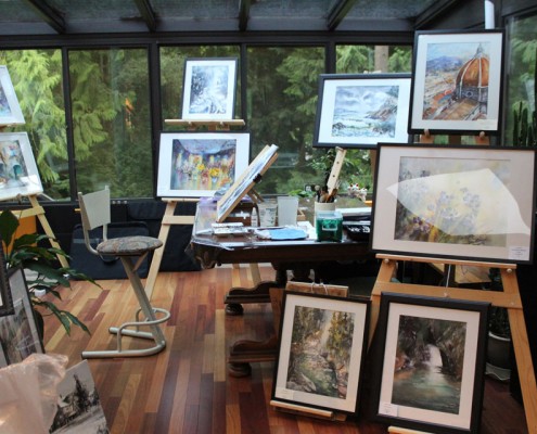 Art studio with paintings on display; windows with a view to trees in the background.