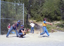 Man in full swing hitting a softball with the catcher and umpire behind him