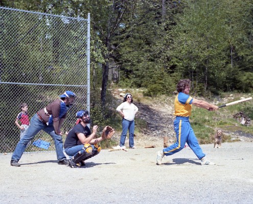 Man in full swing hitting a softball with the catcher and umpire behind him
