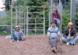 Four men sitting in a playground next to a set of monkey bars, a baseball glove is hanging from the bars.