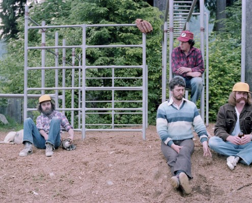 Four men sitting in a playground next to a set of monkey bars, a baseball glove is hanging from the bars.
