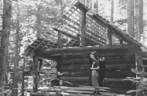 Woman standing on the deck of a cabin under construction. Trees in the background.