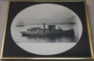 Black and white framed photograph of a tugboat with three people on deck.