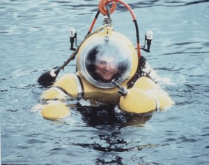 Man partly submerged in water wearing a yellow atmospheric diving suit.