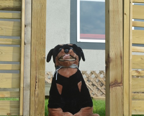 Black and brown stuffed dog sitting in a gap in a fence.