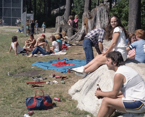 People gathered at a park sitting along the sidelines to watch a softball game.