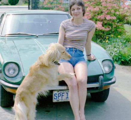 Woman leaning against the hood of her car with a dog jumping up onto her.