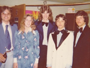 Four young men and one young woman standing together in 1970s formal attire.