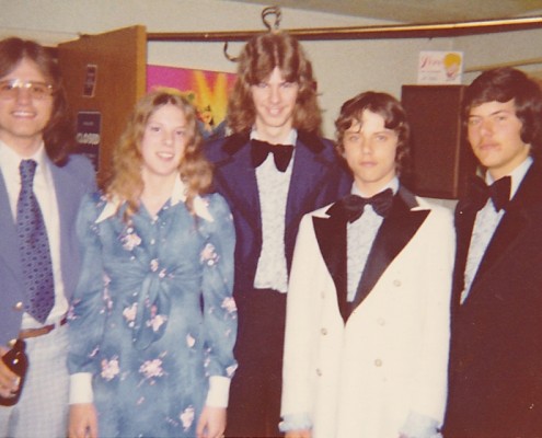 Four young men and one young woman standing together in 1970s formal attire.