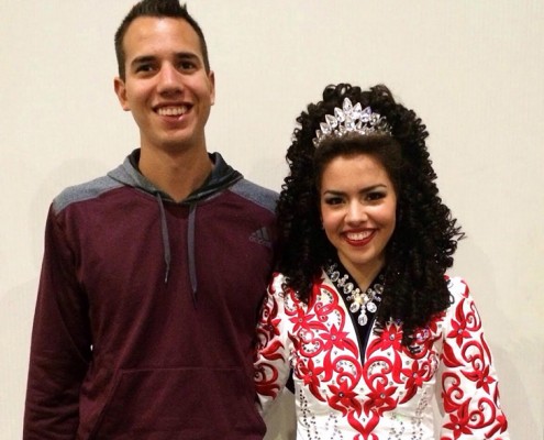 Teenage girl wearing a silver crown and Irish dance costume standing next to her brother.