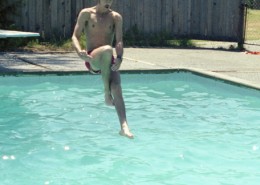 Man jumping from a diving board into an outdoor swimming pool.