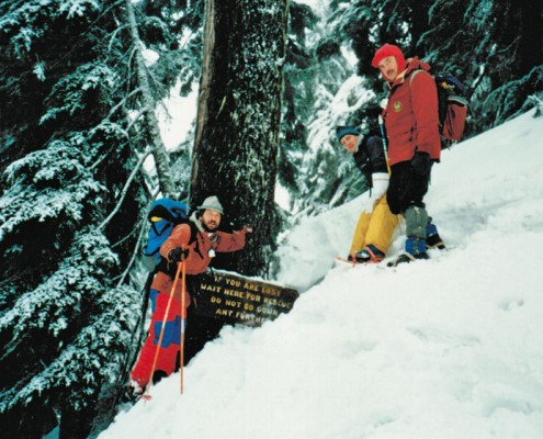 Three members of the NSR on a mountain slope next to sign that reads: If you are lost, wait here for rescue. Do not go down any further.