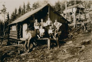 Group of people gathered on the porch of a cabin holding signs, a second cabin can be seen in the distance.
