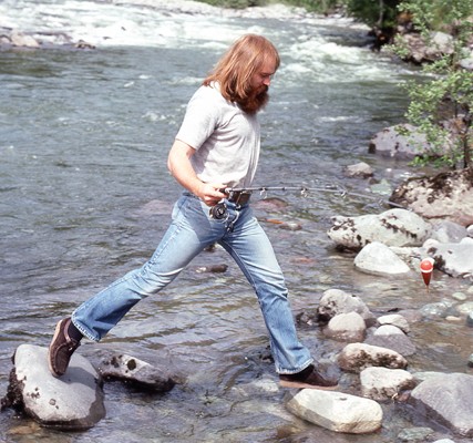 Man with fishing rod stepping from one rock to another in a stream. 5tags: photography, North Vancouver, Lynn Valley, Bruce Flanagan, softball, archives