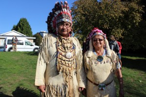 Two people wearing regalia, including headdresses, standing together in a park.