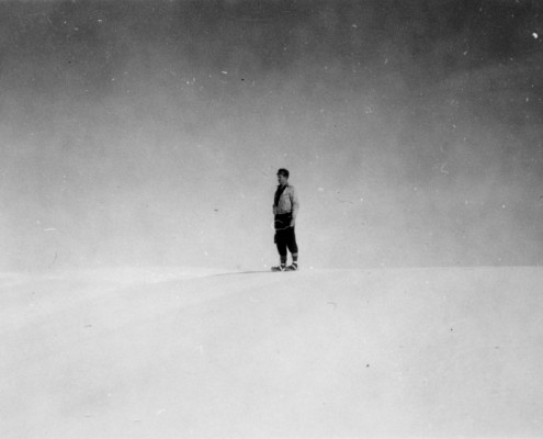 Distant view of a man standing on snow-covered hill with a stark background.