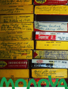 Stack of a variety of yellow square video reel boxes with handwritten titles and notes.