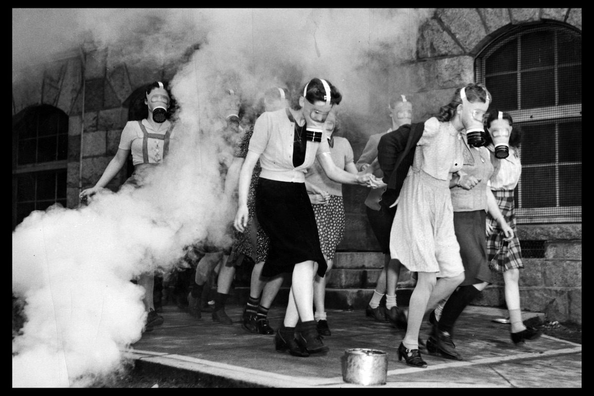 Girls leaving Queen Mary School during a gas mask drill, ca. 1941. A simulated gas was used for this exercise. Girl in the centre of the image, in dark dress and light sweater, is Leonora Hutchinson.