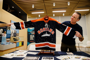 Hockey historian Chris Mizzoni at MONOVA: Museum of North Vancouver next to a replica Norvans sweater, 23 April 2022. Photo: Alison Boulier