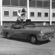 Jack Cash and camera/tripod mounted on top of a Buick automobile outside the Empire Pool at University of British Columbia, 1955. NVMA 10432