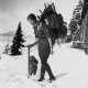 Phyllis Munday with 25 kg pack and ice axe, ca. 1923. Her daughter Edith stands beside her. Cabin can be seen on right. NVMA 5652